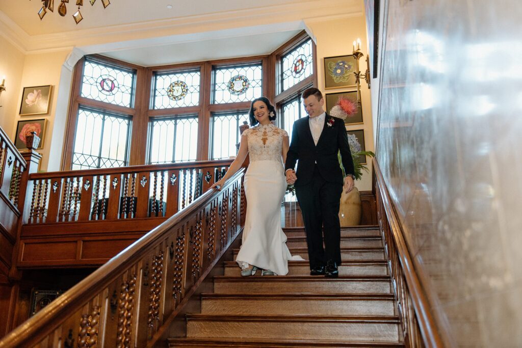 Bride and groom walking down the stairs at Harwelden Mansion hand in hand 