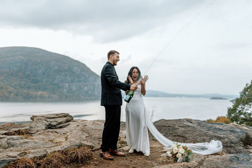 Bride and groom popping champagne on the mountain top in the Hudson Valley