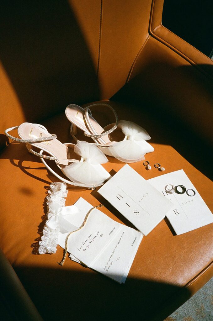 Flat lay detail photography with vows book, rings, and bow shoes on film