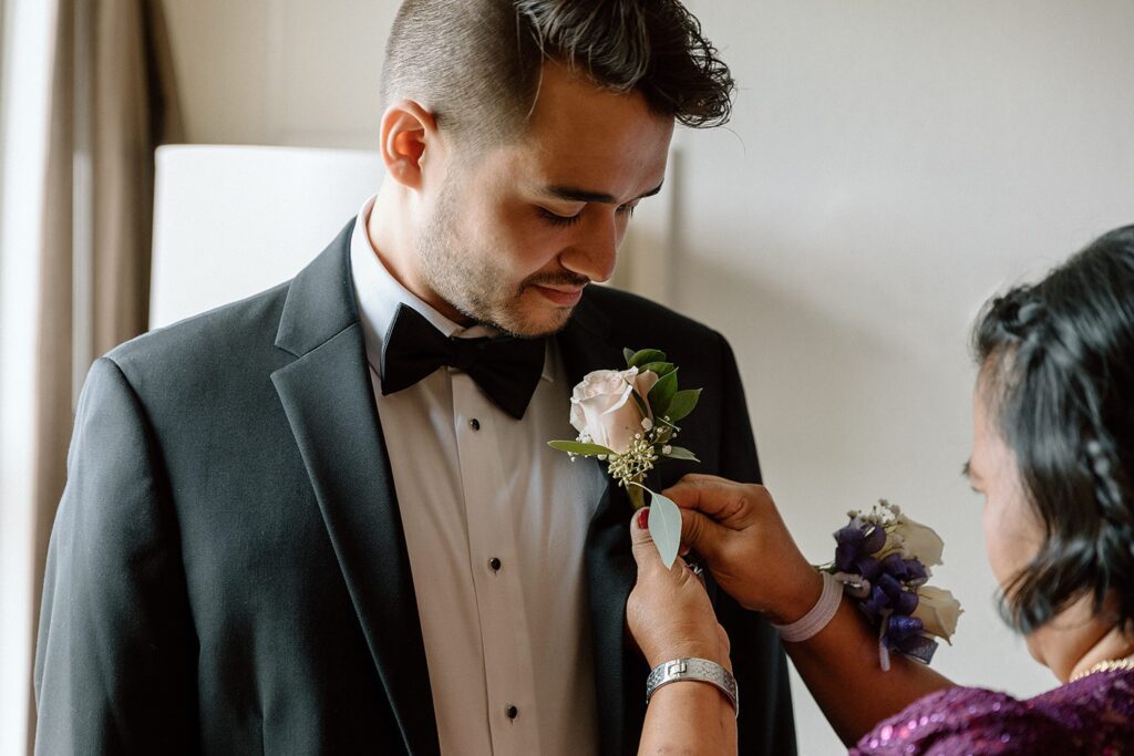 Groom's mom putting on boutonniere for intimate chapel wedding ceremony