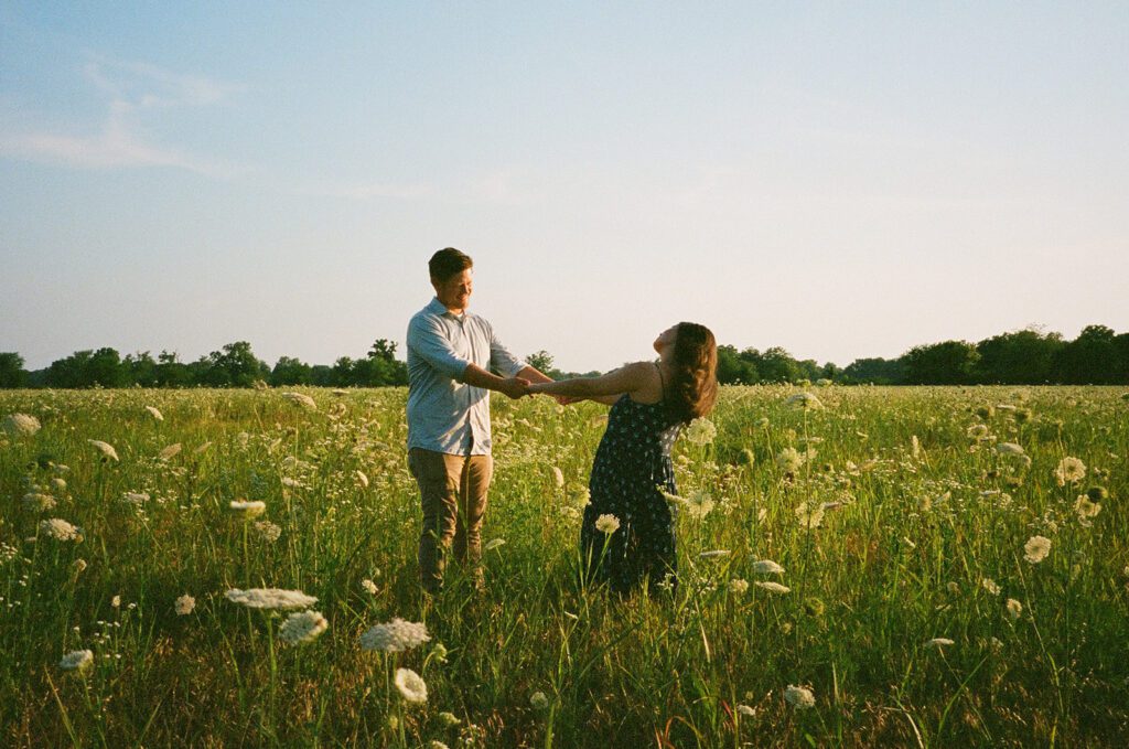 man and woman spinning around in wildflower engagement session in film