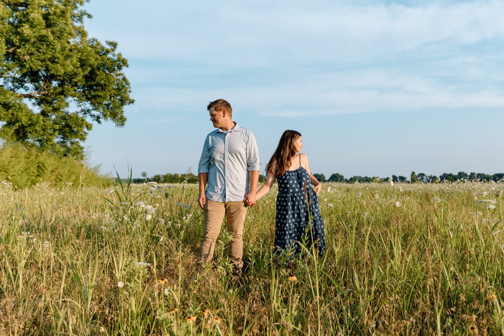 Couple in field staring in opposite directions wildflower engagement session