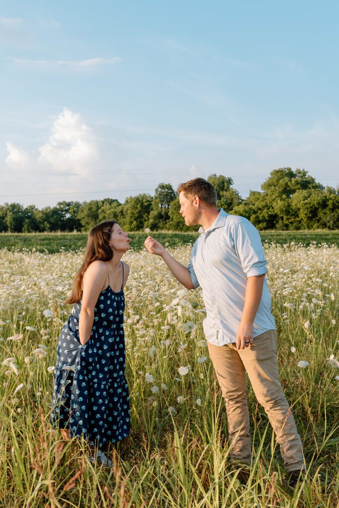 couple blows on wildflower in wildflower engagement session film 