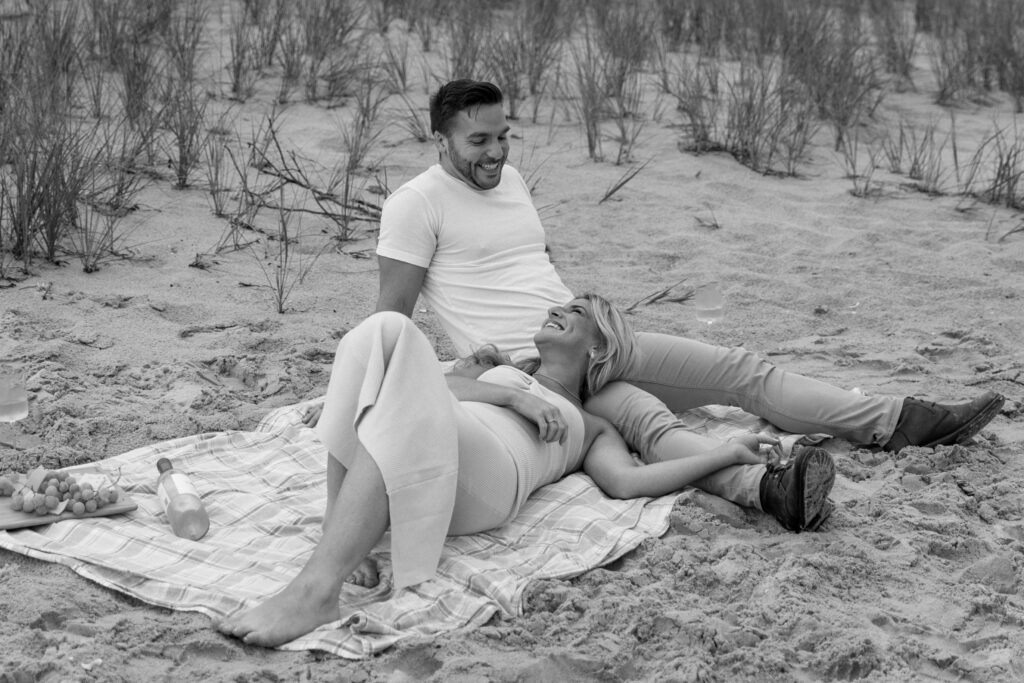 couple laying at a picnic on the beach with tall grass behind them