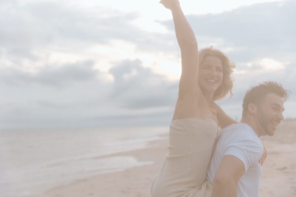 women raising her arm piggyback on a man on the beach 