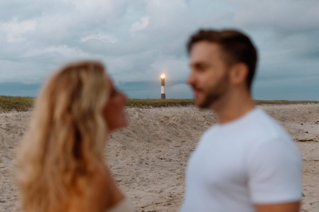 couple on the beach with lighthouse in the distance 