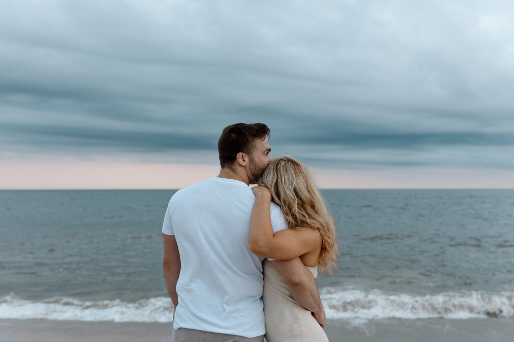 couple embracing in front of the ocean at sunset with storm 