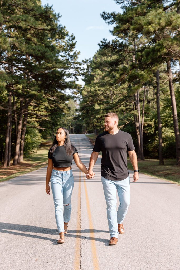 interracial couple holding hands on road in jean and black t-shirt with forest