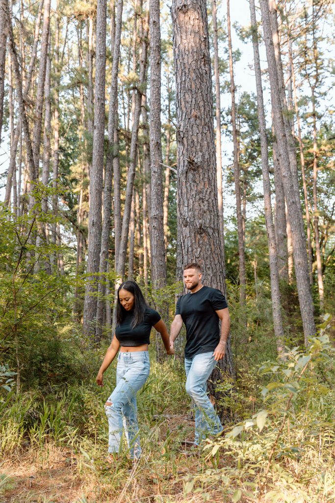 couple walks through forest holding hands in jeans 