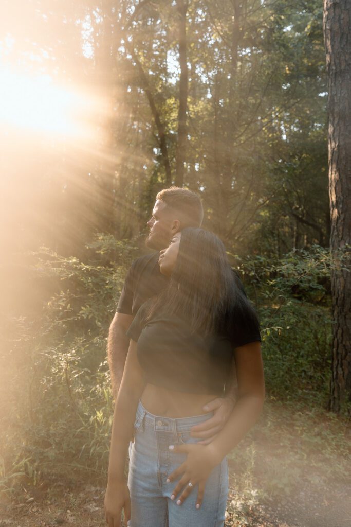 engaged couple in sun rays in forest 