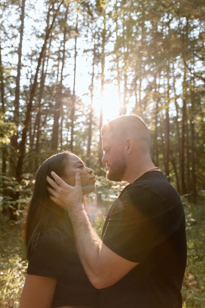 man holds woman's face in forest with sun rays 