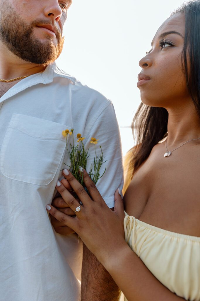 couple looks at each other with wildflowers and engagement ring 