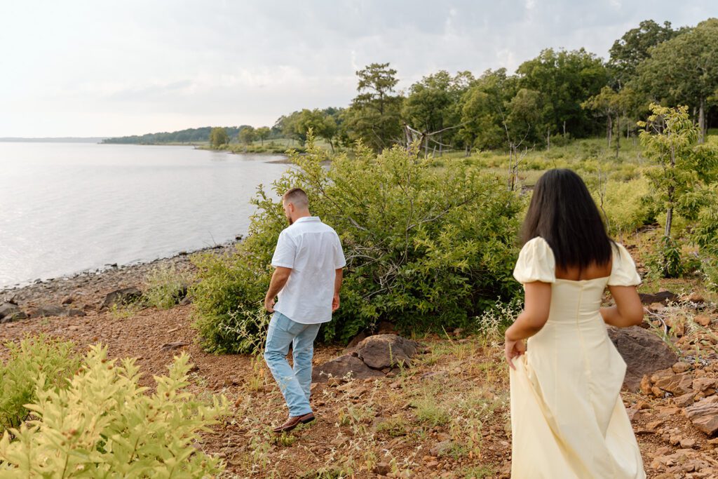 man and woman walk towards shore of lake 