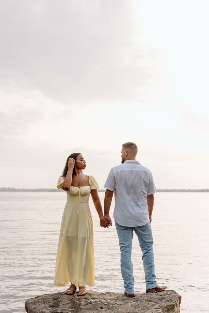 woman and man on rock in lake holding hands 