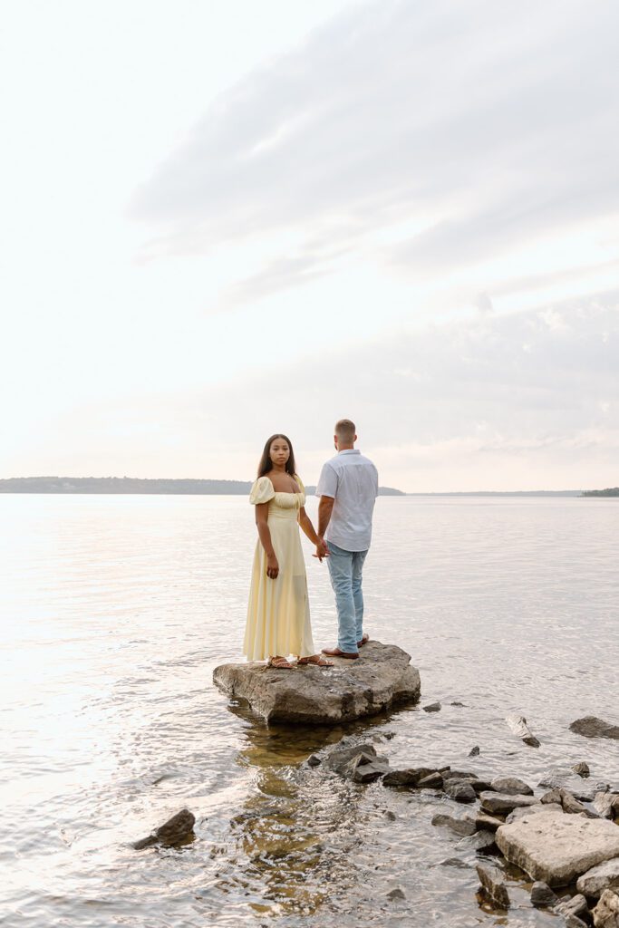 couple on rock in lake holding hands women stares at the camera 