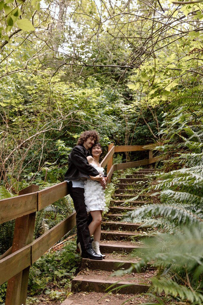 man hugging woman from behind on forest steps at engagement session at Olympic State Park