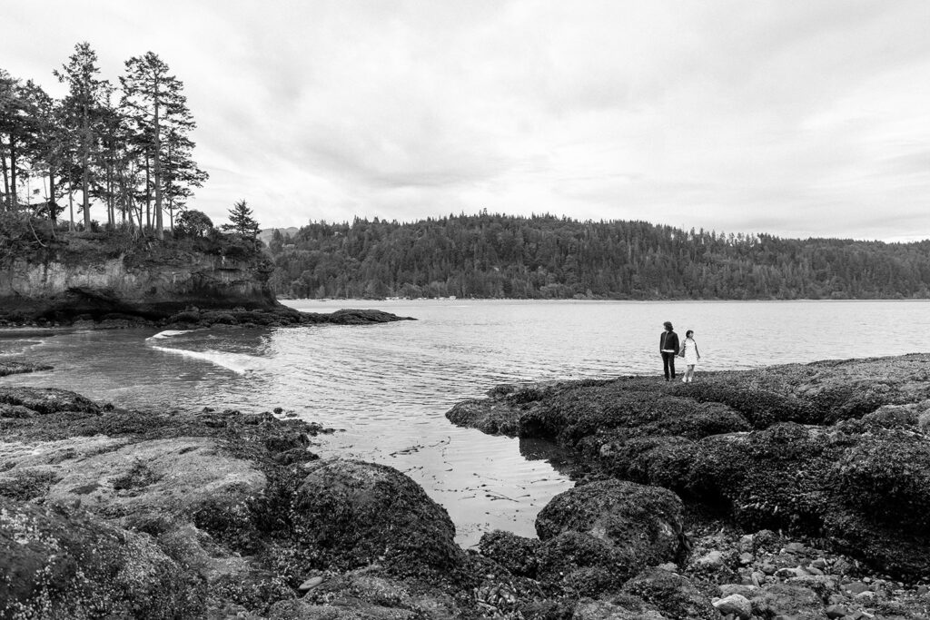 black and white wide shot of couple on rocks in glacial lake Olympic national Park 