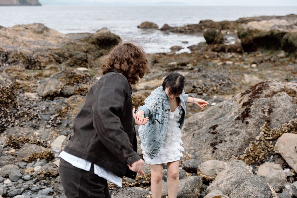 groom helps bride through rocks on shore at olympic national park engagement elopement session PNW