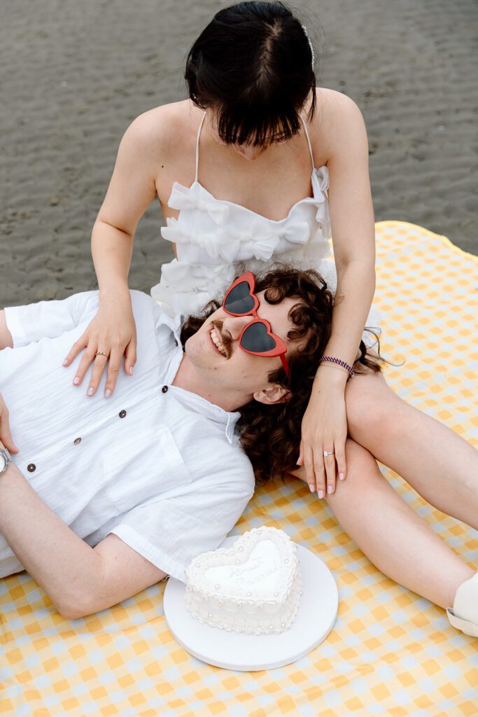 groom with red heart sunglasses and bride with just married cake on gingham picnic blanket PNW elopement 