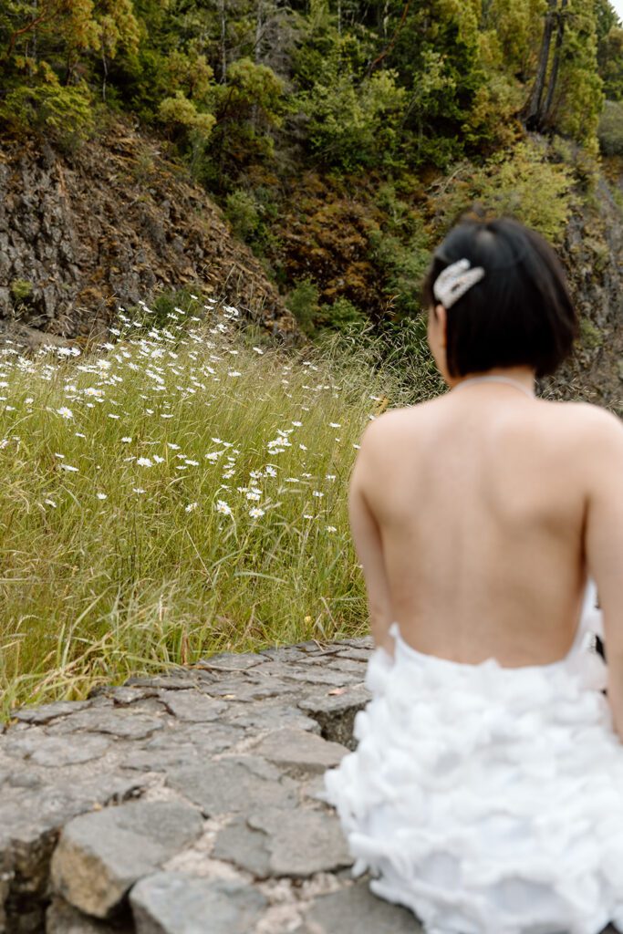 bride sits on rock and looks at wild flower meadow at Olympic National Park 