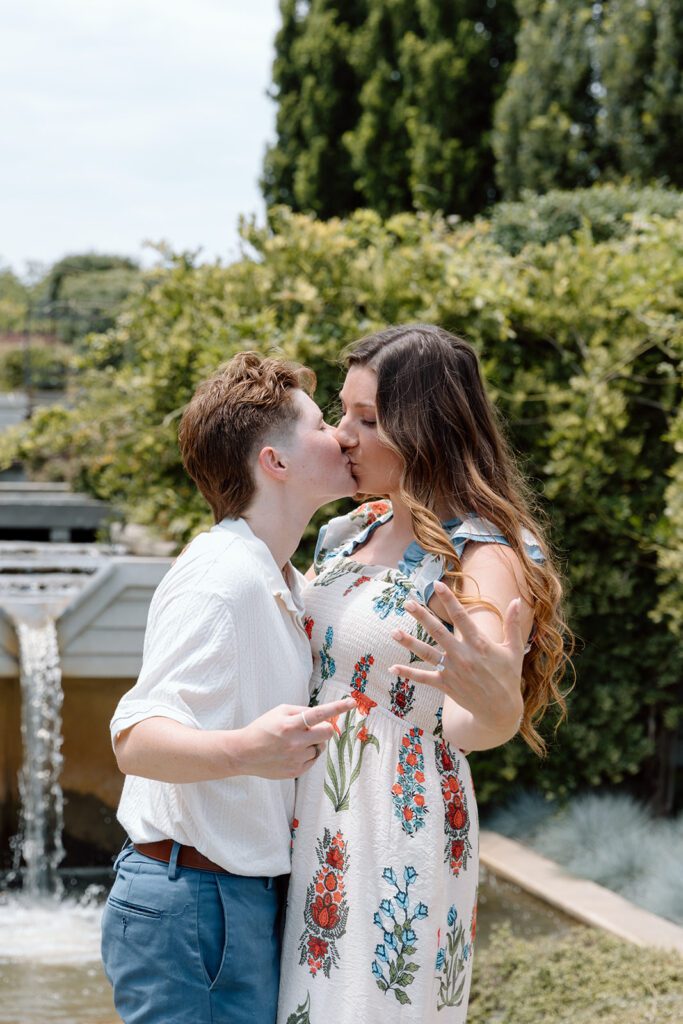 couple kisses and points at ring at queer engagement at Tulsa Botanical Garden