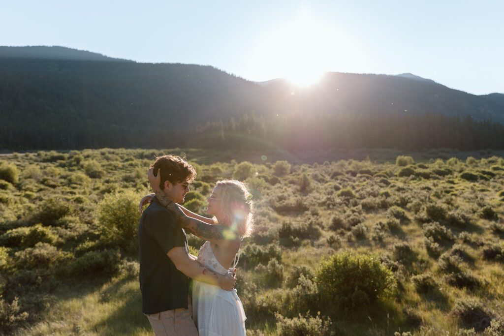 tattooed boho bride holds grooms head as sunsets over mountains 