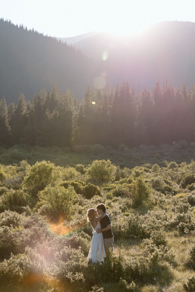 golden hour in a field with mountain backdrop wedding elopement portrait couple holds each other 