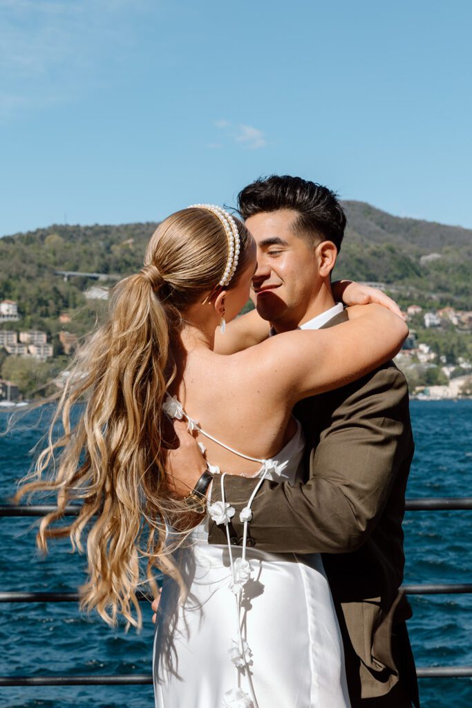 groom smiles at bride and hugs by italian lake 