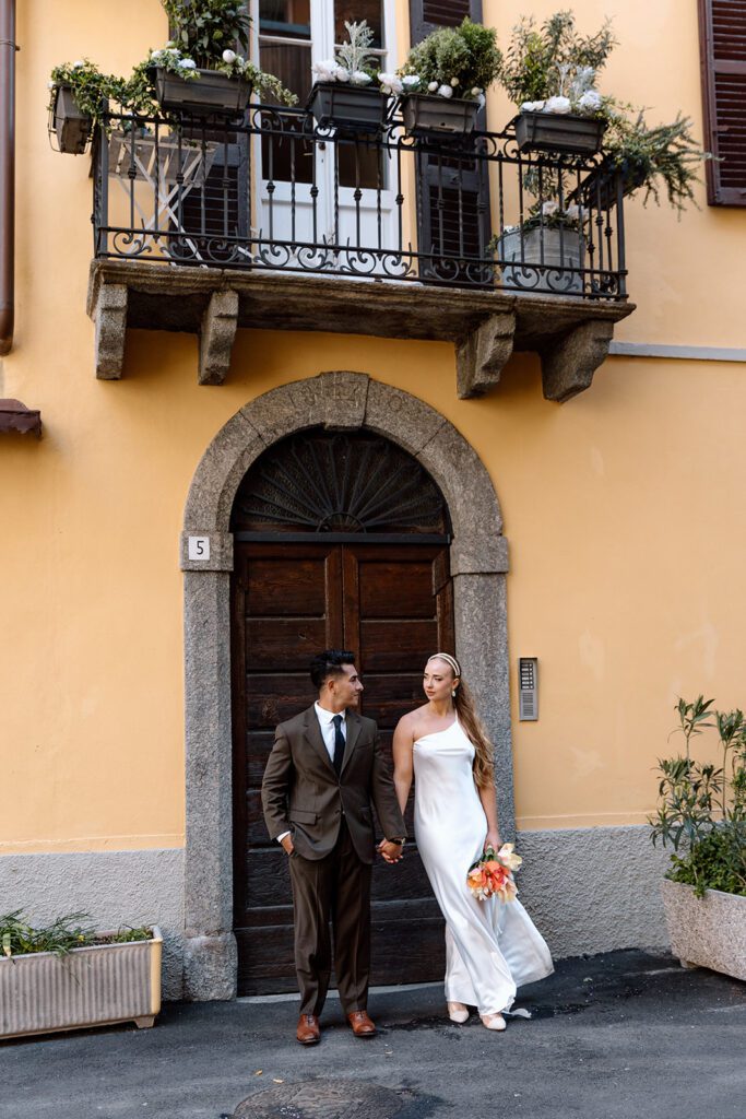 bride and groom in front of Italian arched door hold hands 