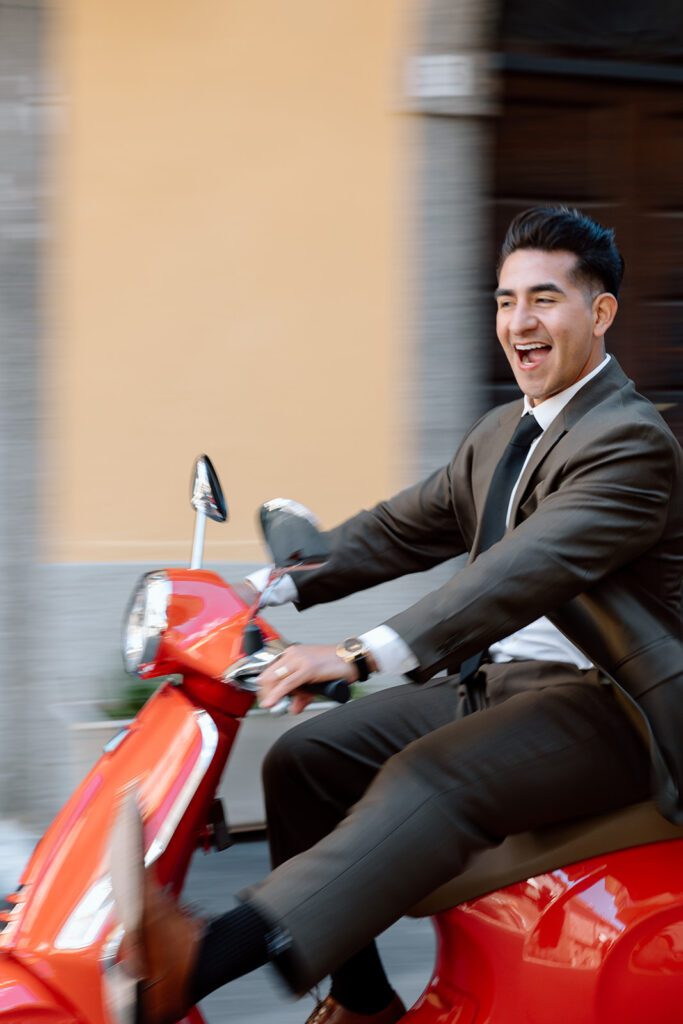 groom cheers and kicks on red vespa 
