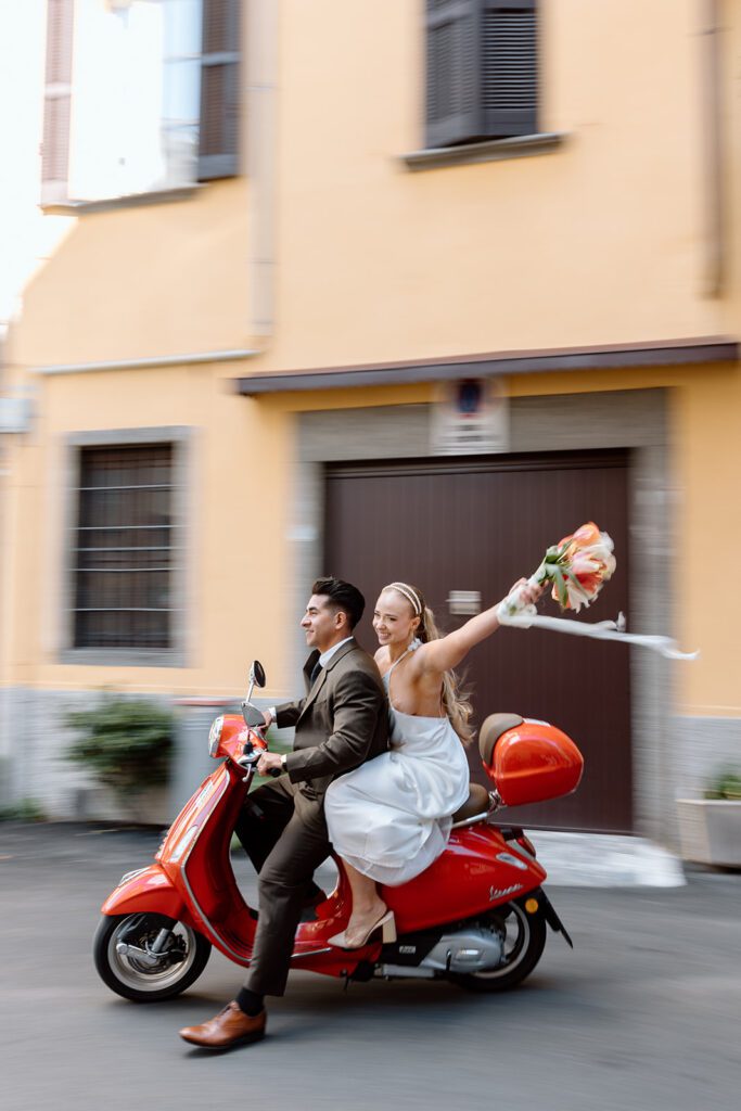 bride waves while groom drives red vespa 