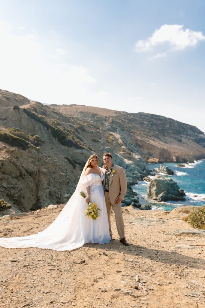 bride and groom stand in front of Mediterranean Sea with yellow bridal bouquet at greek elopement