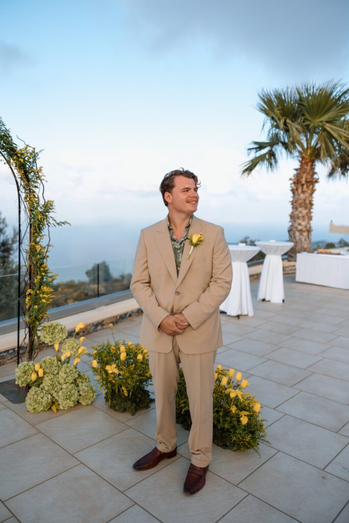 groom stands at flower arch waiting for bride to walk down the aisle 