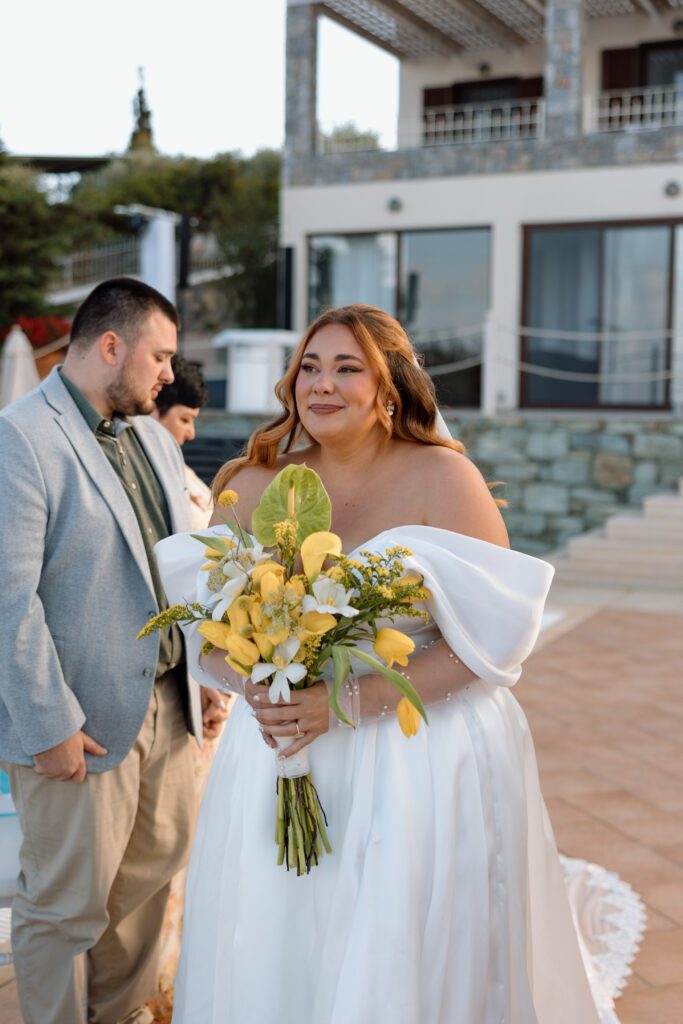 plus size bride beams at groom as she walks down the aisle with yellow tulip bouquet 