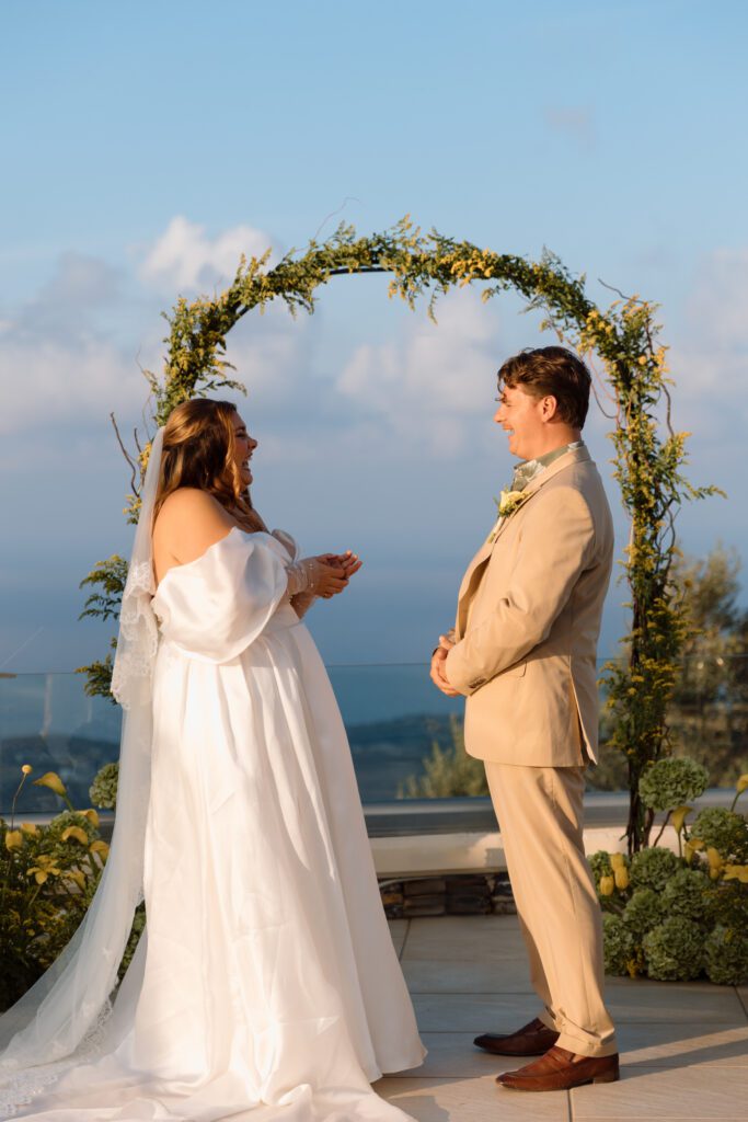 bride and groom laugh over vows with green and yellow arch behind them 