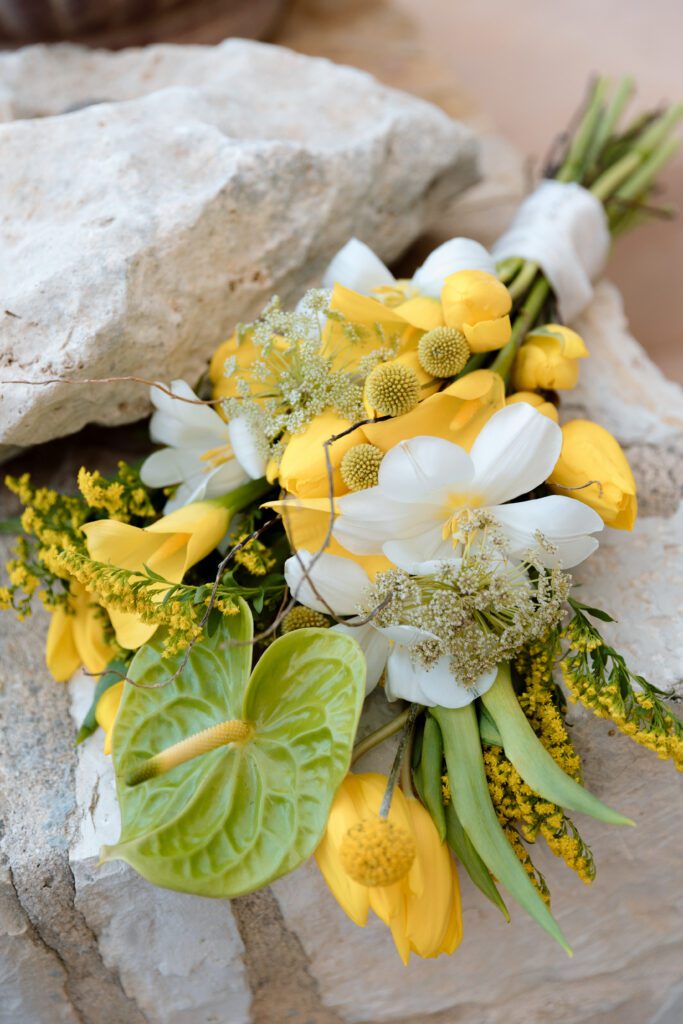 bridal bouquet with green anthuriums, yellow and white flowers sitting on rocks 