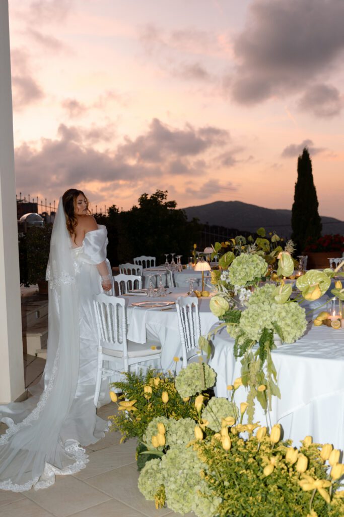 bride poses by reception tables and floral arrangements as the sunsets over the mountain 