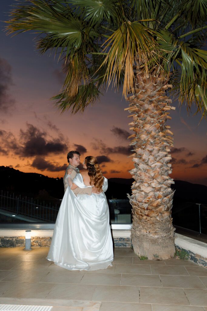 bride and groom dance under palm tree at sunset 